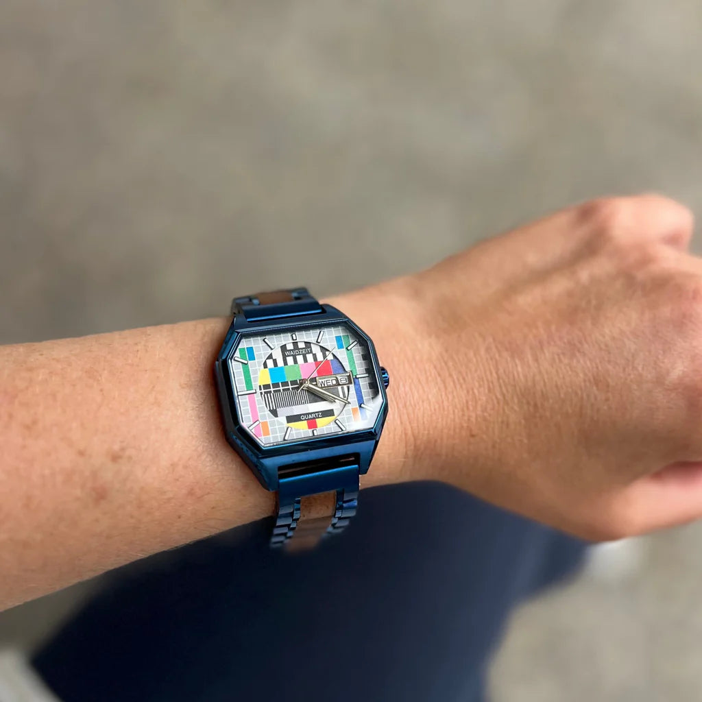 Drevené hodinky Waidzeit Sendeschluss s motívom testovacieho obrazca a modrým náramkom na ruke – originálny dizajn s nostalgiou